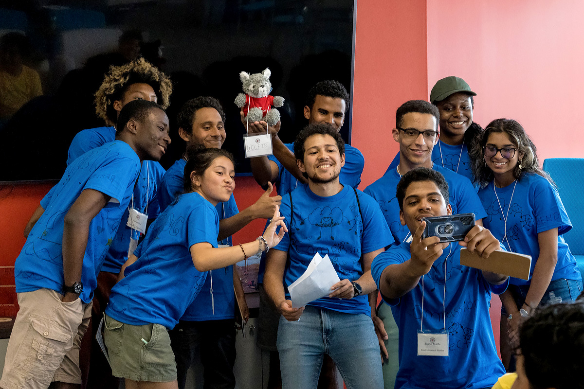 students all wearing blue shirts gather to take a photo with a cellphone