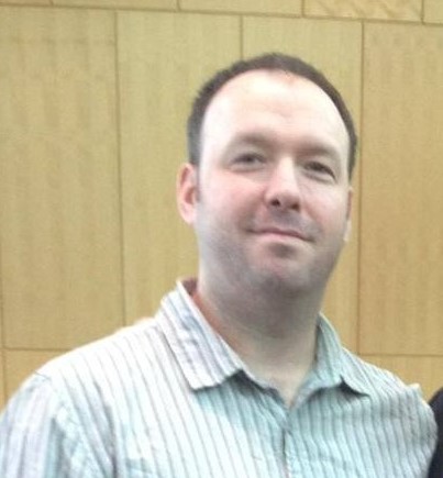 Person in a striped shirt smiling, standing in front of a wooden panel background.