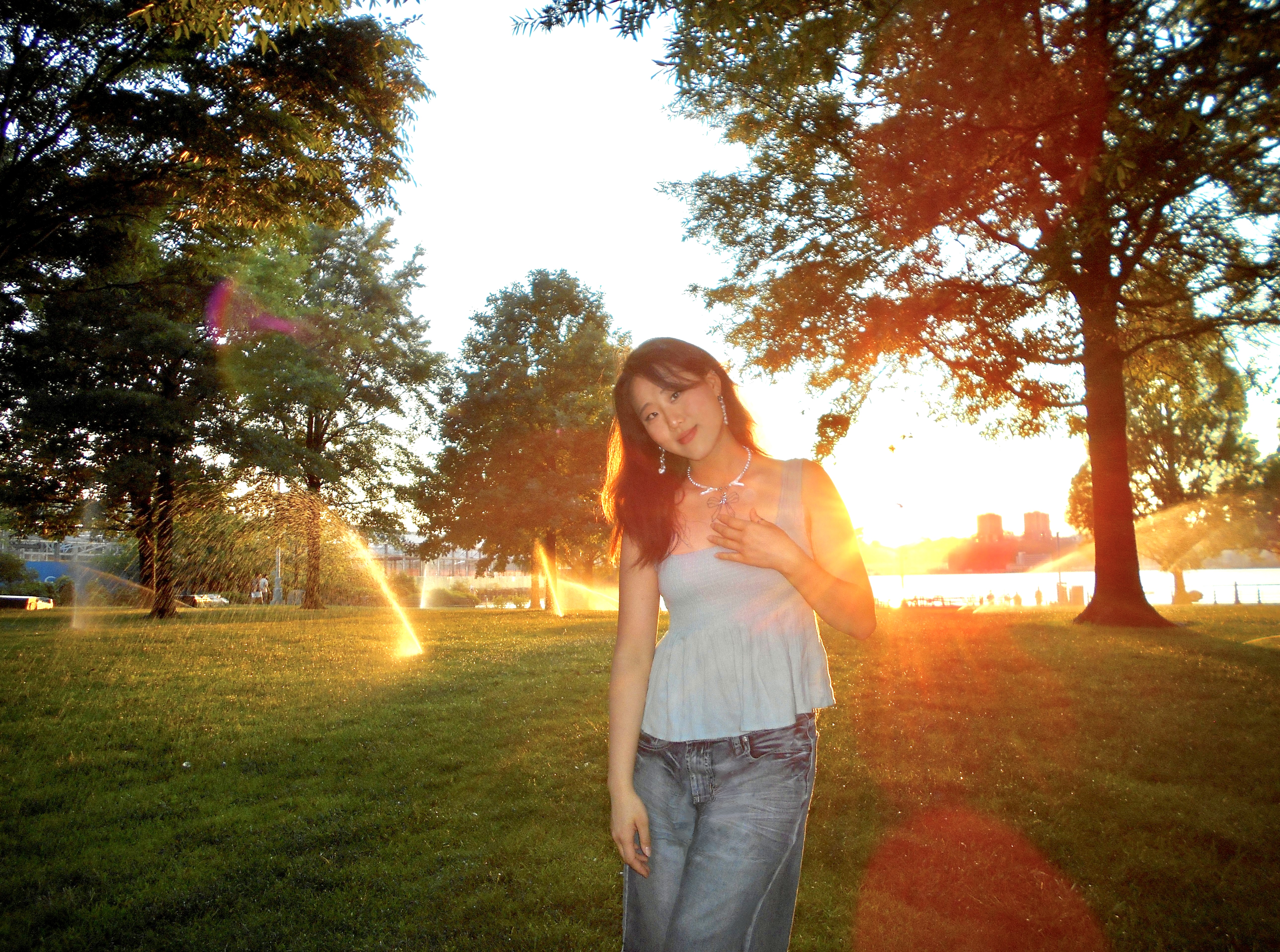 A person smiling, standing outdoors in front of a sunset 