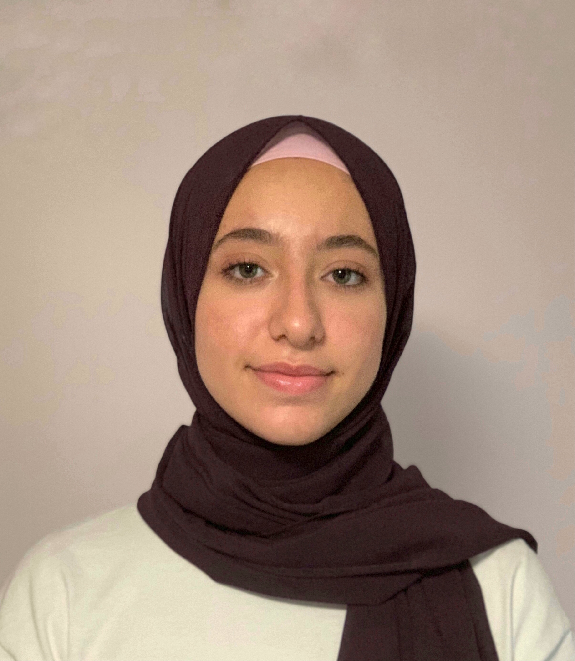 Portrait of a smiling person wearing a brown hijab against a neutral background.