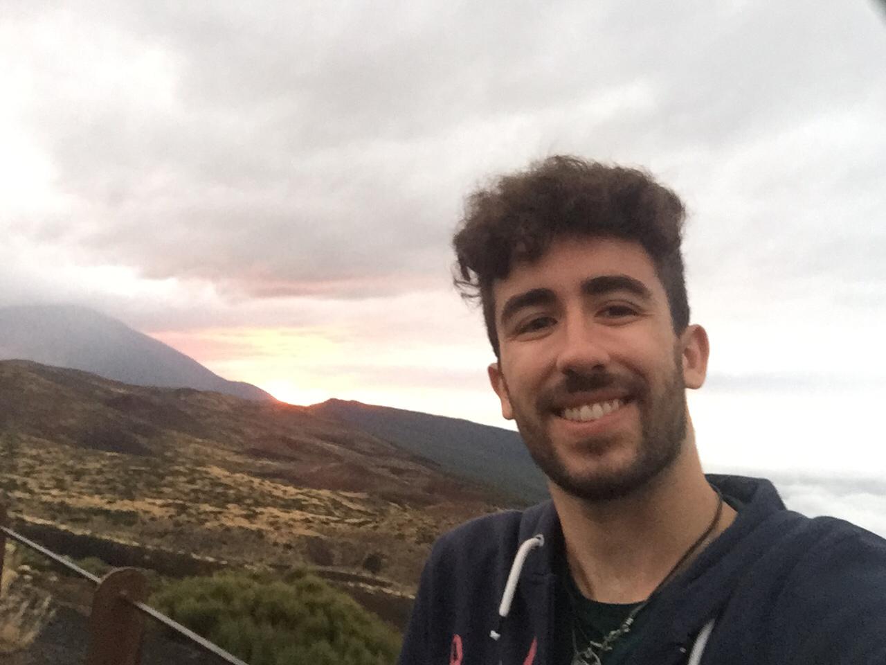 Person smiling for a selfie with a scenic sunset background over volcanic landscapes, possibly near Mount Teide.